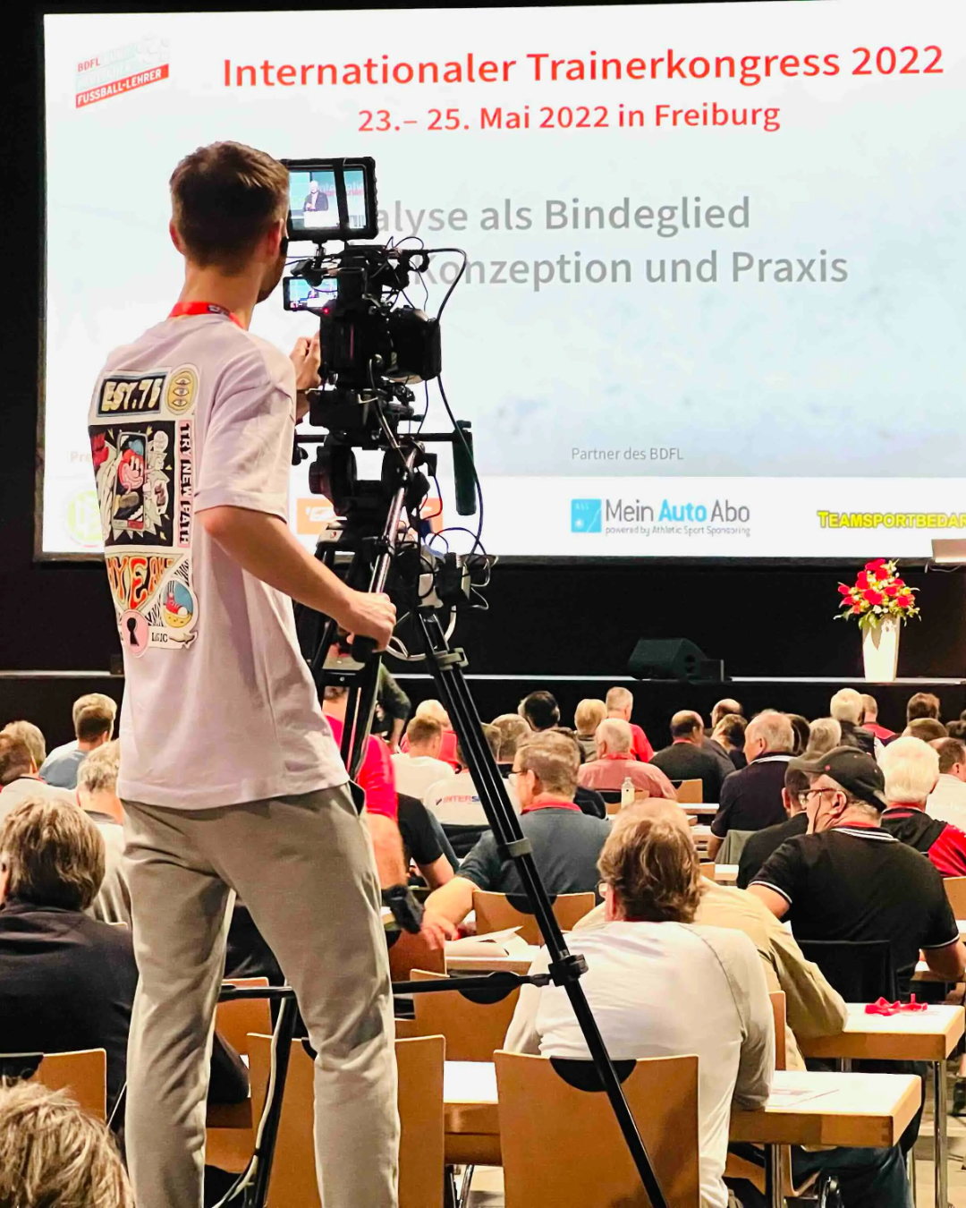 Back of a man at a concert. Hes wearing a beanie hat and a baggy denim jacket with studs. Photo with a purple hue